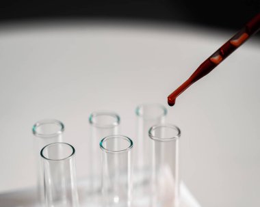 Laboratuvar asistanının, pipetten kan damlatarak test tüpüne kan damlattığı yakın plan.