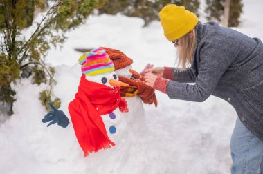 Beyaz kadın kardan bir kardan adam heykeli yapıyor. Havuç burnun yeridir.