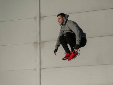 Kapüşonlu beyaz adam elleri dışarıda dizlerinin üzerinde yükseğe zıplıyor.