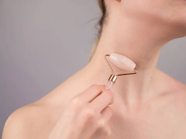 Close-up portrait of a woman using a quartz roller massager for an alternative fight against wrinkles on her neck. Smoothing of the rings of venus
