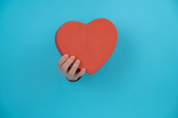 A womans hand with a heart-shaped gift box sticks out of a blue paper background