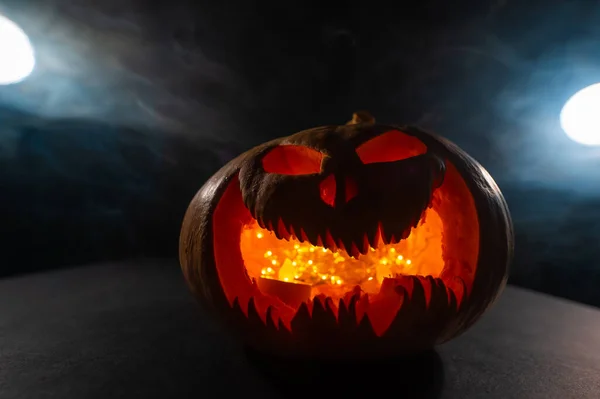 A creepy pumpkin with a carved grimace in the smoke. Jack o lantern in the dark