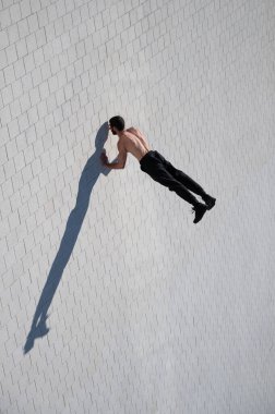 Tişörtsüz bir adam dışarıda elini kolunu sallayarak yürüyor. Yukarıdan görüntüle