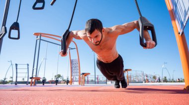 Tişörtsüz adam dışarıda ilmek egzersizi yapıyor.