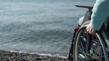 Deniz kıyısında tekerlekli sandalyedeki beyaz kadın. Kadın ellerine yakın çekim