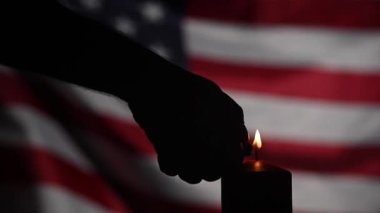 Bir adam karanlıkta Amerika Birleşik Devletleri bayrağının arka planında bir mum yakıyor. Yavaş çekim