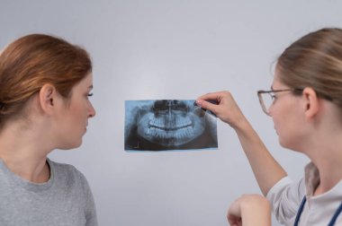 Resepsiyondaki bir kadın doktor ve bir hasta çene röntgenini tartışıyorlar.