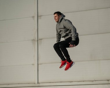 Kapüşonlu beyaz adam elleri dışarıda dizlerinin üzerinde yükseğe zıplıyor.