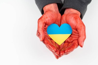 Elleri kana bulanmış bir kadın beyaz arka planda Ukrayna bayrağı taşıyan bir kalp tutuyor.