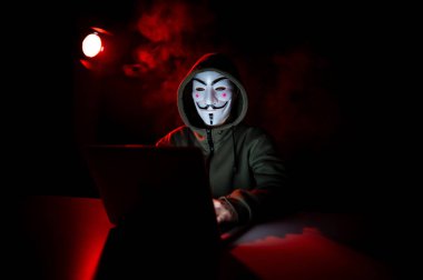 5 Haziran 2022 Novosibirsk, Rusya: Kapüşonlu Anonymous kırmızı dumanlı bir laptopta yazı yazıyor