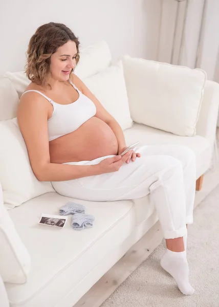 Zwangere Vrouw Zit Een Witte Bank Houdt Een Smartphone Foetale — Stockfoto