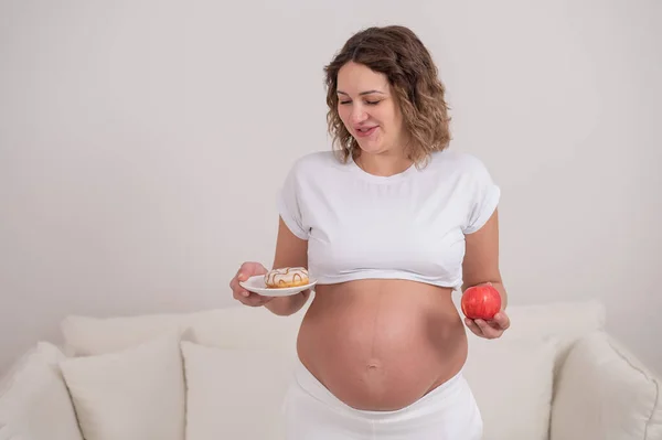 Беременная Женщина Держит Красное Яблоко Пончик Выбор Продуктов Питания — стоковое фото