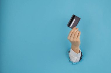 Bir kadının eli kağıtta bir delikten dışarı sarkan mavi arka planda bir kredi kartı tutar.