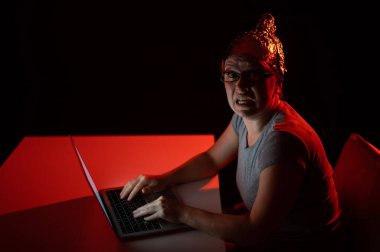 Alüminyum folyo kapaklı bilgisayarda yazan paranoyak beyaz kadın. Komplo teorisi