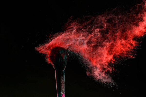 Makeup brush with an explosion of red powder on a black background