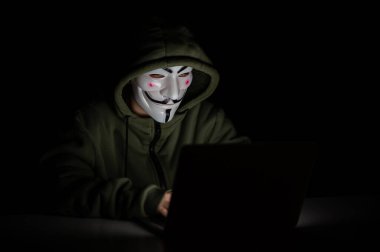 Kapüşonlu anonim karanlıkta dizüstü bilgisayarda yazıyor.