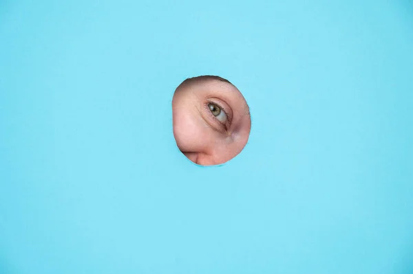 Woman peeking out of hole in blue paper background
