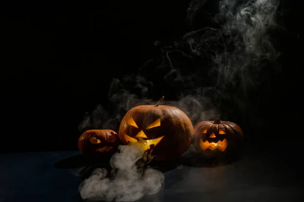 Pumpkins with carved grimaces and candles inside in the dark for halloween. Jack o latern in smoke