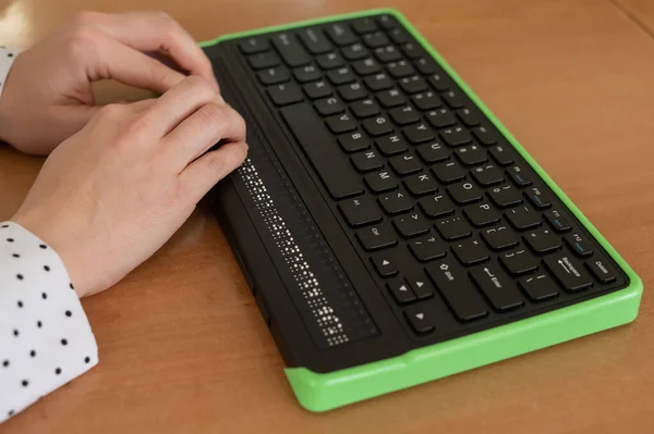 A blind woman uses a computer with a Braille display and a computer keyboard. Inclusive device