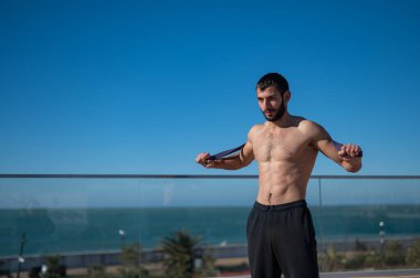 Tişörtsüz adam dışarıda lastik bantlarla egzersiz yapıyor.