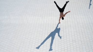 Tişörtsüz bir adam dışarıda elini kolunu sallayarak yürüyor. Yukarıdan görüntüle