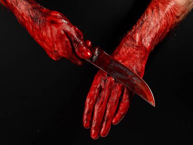 Bir adam kanlı bir bıçağı siyah bir arka planda siliyor.