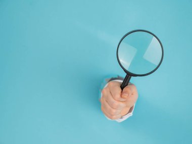 Kağıt mavisi arka planda bir delikten dışarı sarkan bir kadının eli büyüteç tutuyor. Boşluğu kopyala