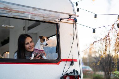Beyaz kadın köpeği Jack Russell Terrier 'a sarılırken minibüsün camından dışarı bakar. Sonbaharda bir karavanla seyahat et.