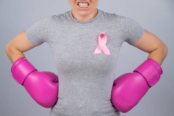 Angry woman in pink boxing gloves with a pink ribbon holds her hands at her hips. Fight against breast cancer