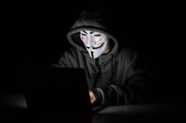 Kapüşonlu anonim karanlıkta dizüstü bilgisayarda yazıyor.