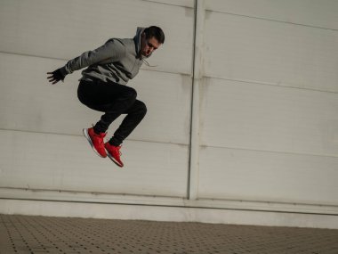 Kapüşonlu beyaz adam elleri dışarıda dizlerinin üzerinde yükseğe zıplıyor.