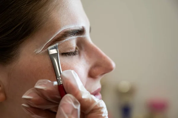 The master draws the shape of the eyebrows with white paint before coloring