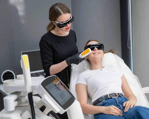 A woman on a couch in goggles undergoing a photorejuvenation procedure. Hardware cosmetology