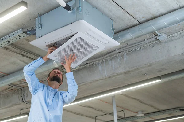 Caucasian bearded man repairing the air conditioner in the office