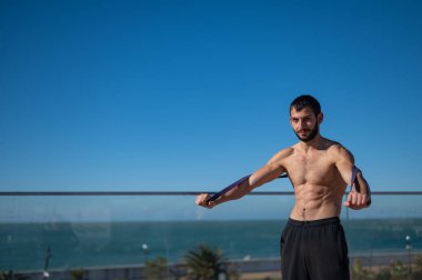 Tişörtsüz adam dışarıda lastik bantlarla egzersiz yapıyor.