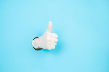 Eldivenli bir kadın, mavi bir kağıttan sarkıyor ve baş parmağını kaldırıyor.