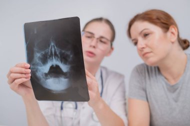 Resepsiyondaki bir kadın doktor ve hasta sinüslerin röntgenini tartışıyorlar.