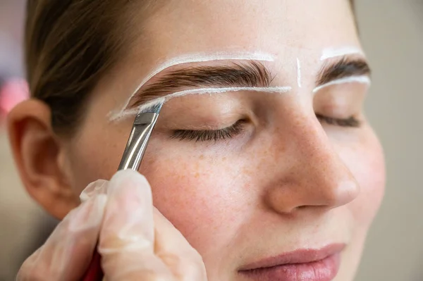 The master draws the shape of the eyebrows with white paint before coloring