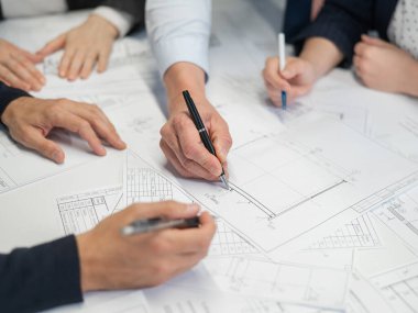 Ofisteki masanın üzerinde planları olan dört meslektaşın ellerinin yakın çekimi. Mühendis ve mimarların beyin fırtınası