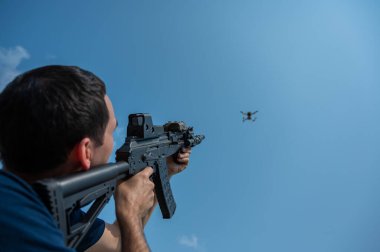 Kafkasyalı bir adam tüfekle uçan bir dronu vuruyor.