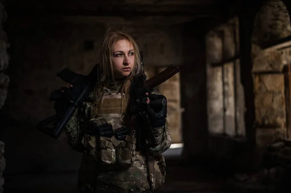 Blonde woman in army uniform holding a firearm in an abandoned building