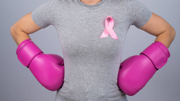 A faceless woman in pink boxing gloves with a pink ribbon holds her hands at her hips. Fight against breast cancer