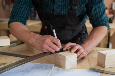Bir marangoz ahşap kalasları ölçer ve atölyede bir kalemle izler bırakır.