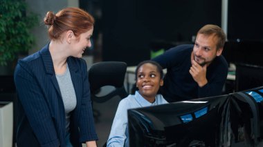 Meslektaşlar monitöre bakar ve çalışma saatlerine karar verir. Afrikalı genç kadın, beyaz erkek ve kızıl saçlı beyaz kadın ofiste iletişim kuruyor.