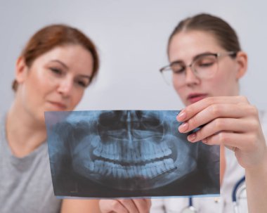 Resepsiyondaki bir kadın doktor ve bir hasta çene röntgenini tartışıyorlar.