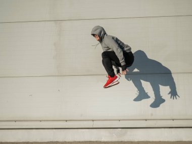 Kapüşonlu beyaz adam elleri dışarıda dizlerinin üzerinde yükseğe zıplıyor.