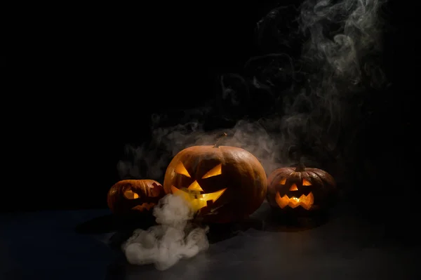 Pumpkins with carved grimaces and candles inside in the dark for halloween. Jack o latern in smoke