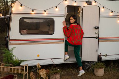 Büyük boy kırmızı örgü kazaklı beyaz kadın sonbaharda karavanla seyahat ediyor.