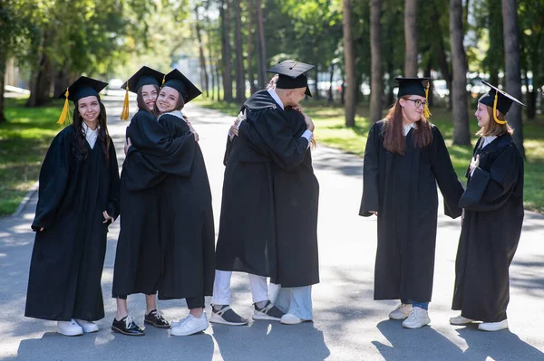 Groep Van Gelukkige Afgestudeerden Gewaden Knuffelen Buiten — Stockfoto