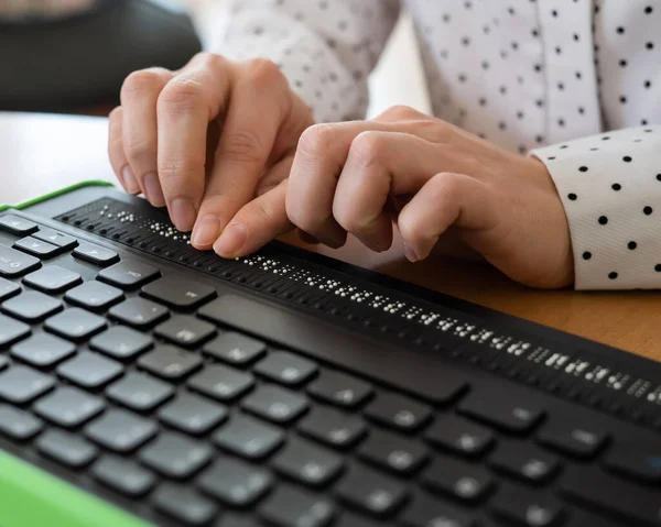 A blind woman uses a computer with a Braille display and a computer keyboard. Inclusive device